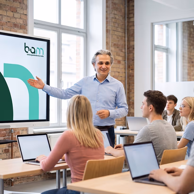Mitat Mola beim unterrichten einer Klasse voller Meisterschüler, auf Präsentation zeigend