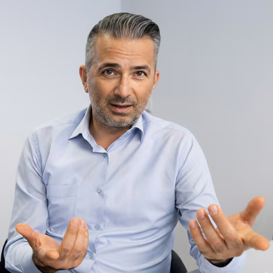 Portraitbild von Mitat Milo, der in erklärender Pose sitzt
